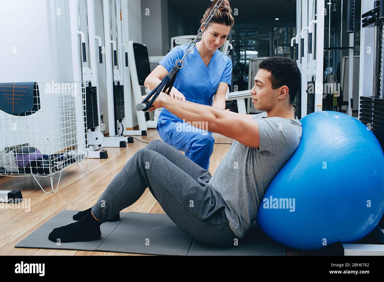le kinésiologue aide un homme de race mixte à faire des exercices pour renforcer ses muscles du dos. traitement de la douleur du dos à l'aide de kinésithérapie. Banque D'Images