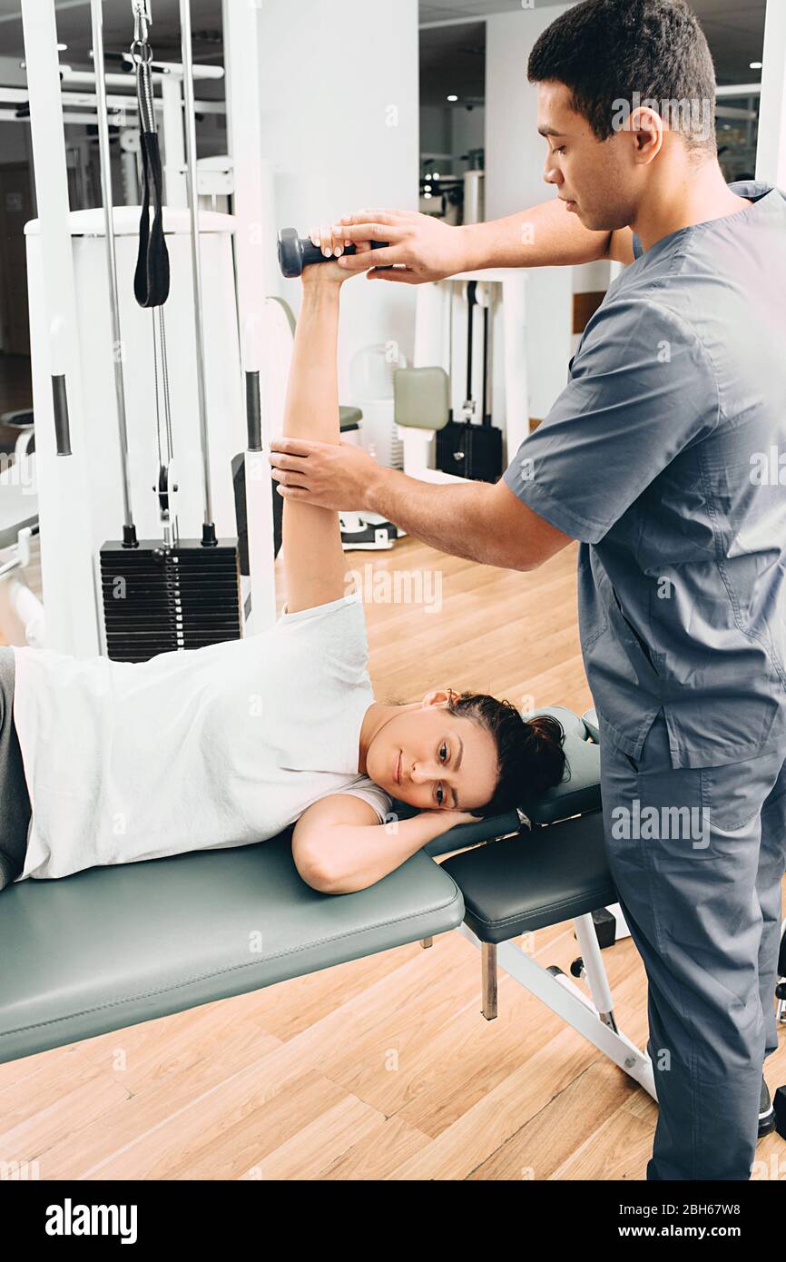la femme dans un centre de réadaptation se trouve sur une table de massage et tient une haltère dans sa main. Exercices pour récupérer d'une blessure. Formateur en réadaptation Banque D'Images