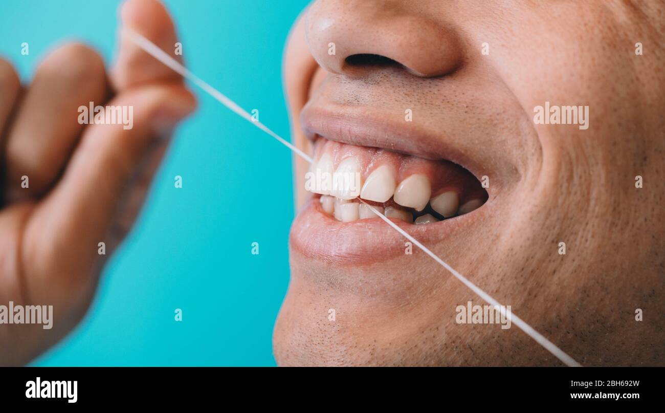 Bouche mâle rapprochée tout en flosant les dents avec fil dentaire sur fond bleu. Hygiène dentaire Banque D'Images