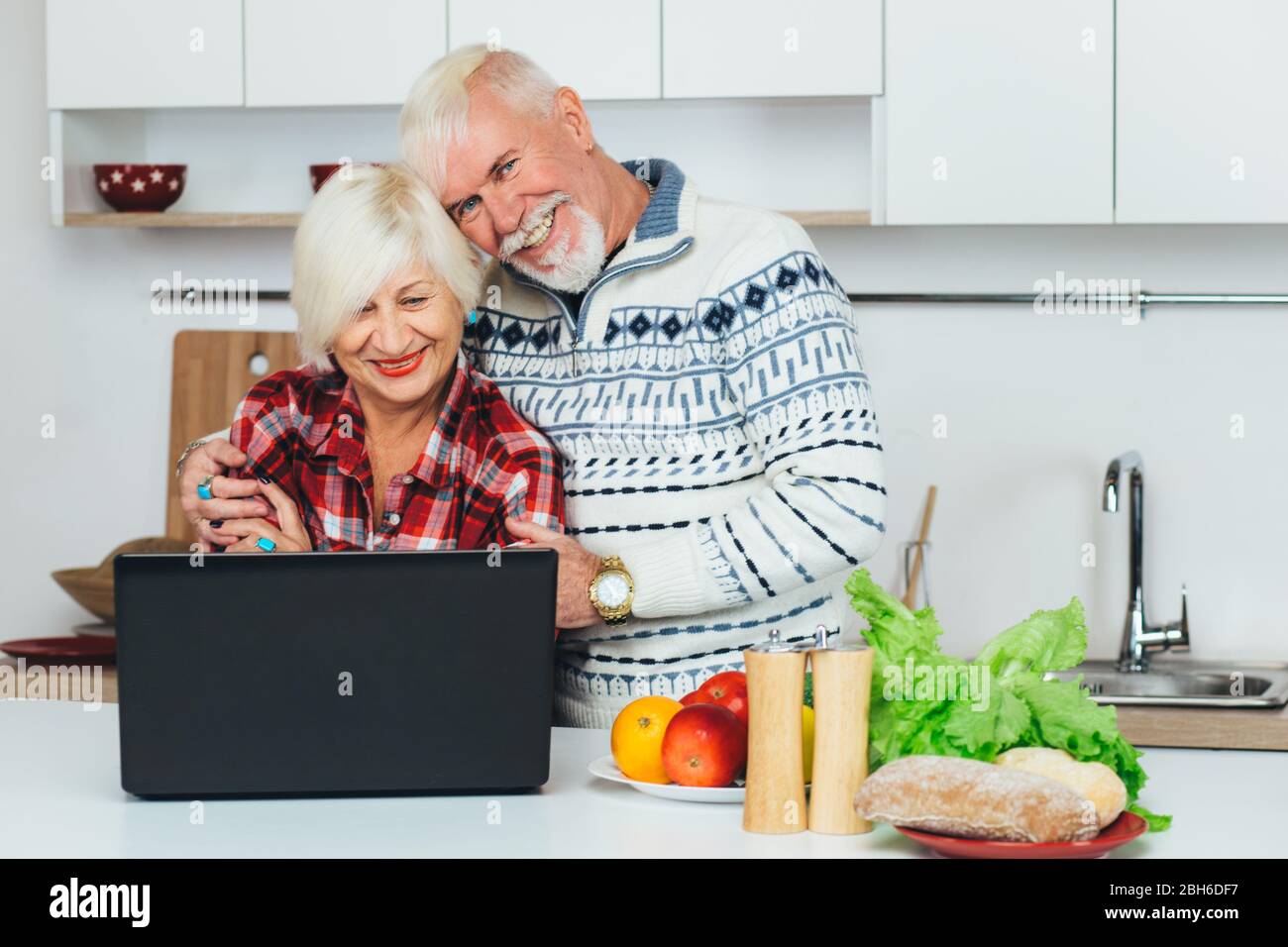 Les personnes âgées, hommes et femmes, recherchent une recette dans un ordinateur portable, préparant des aliments sains à la maison, dans la cuisine Banque D'Images