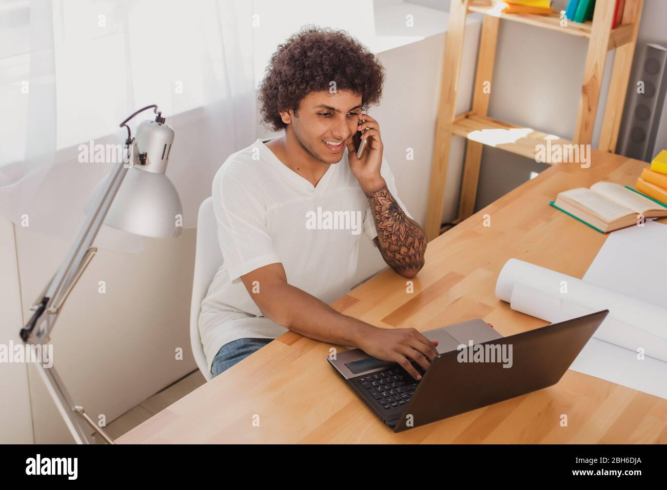 Positif et maudit, homme parlant émotionnellement sur le téléphone mobile tout en étant assis à son lieu de travail à la maison, surfer sur Internet, sur son ordinateur portable. Banque D'Images
