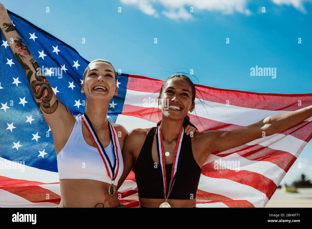 Deux athlètes féminins tenant le drapeau américain à l'extérieur. Les coureurs américains de femmes célèbrent la victoire sur la piste de course au stade. Banque D'Images