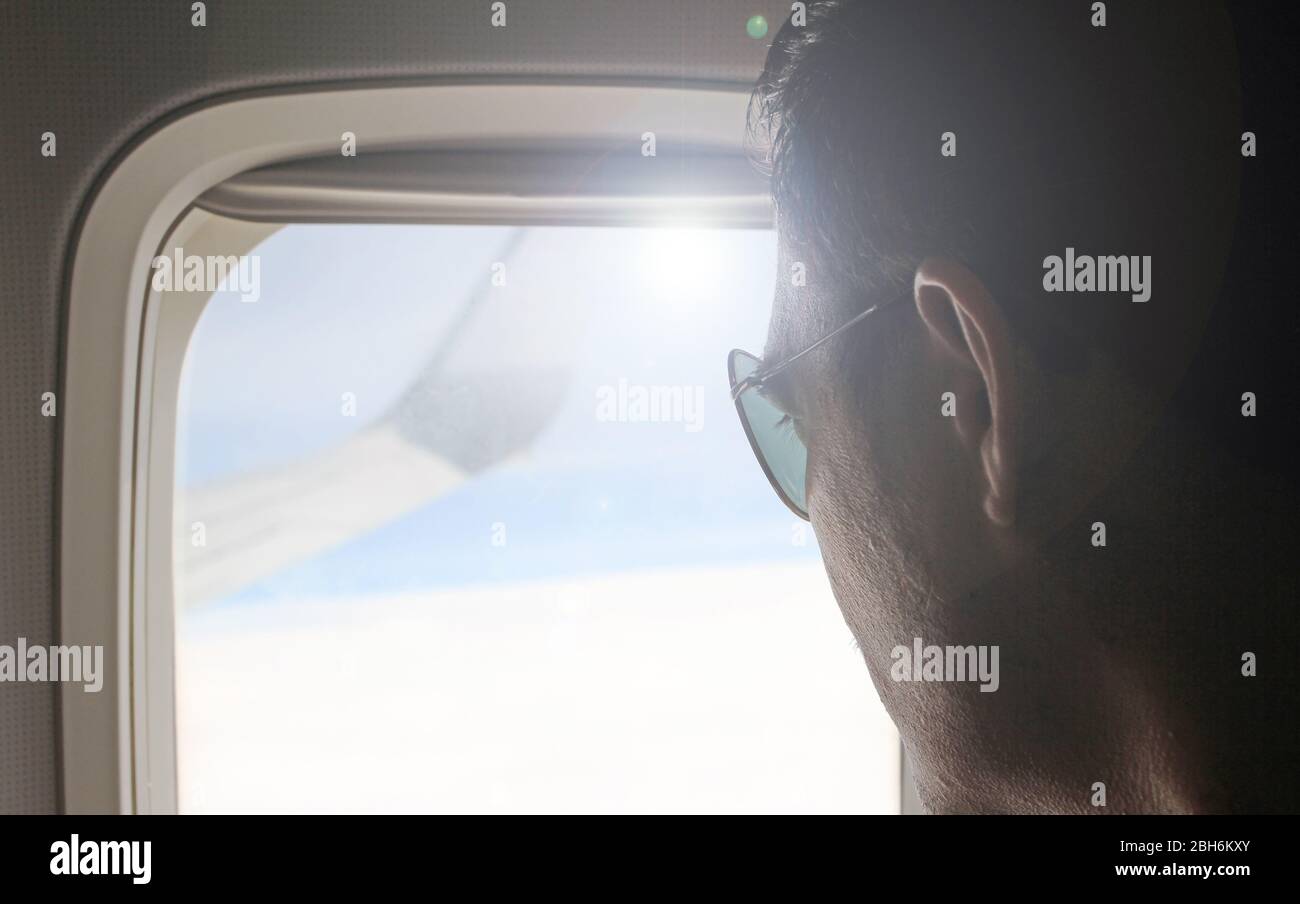 Jeune passager regardant par la fenêtre de l'avion volant. Vue latérale de l'homme de main contre la fenêtre de l'avion assise et regardant dehors. Wanderlust. Banque D'Images