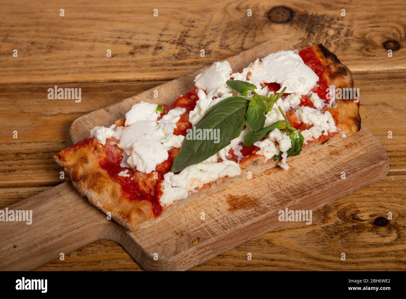 Cuisine italienne.tranche de pizza rectangulaire maison avec basilic, mozzarella de buffle fraîche et tomates sur planche en bois. Banque D'Images