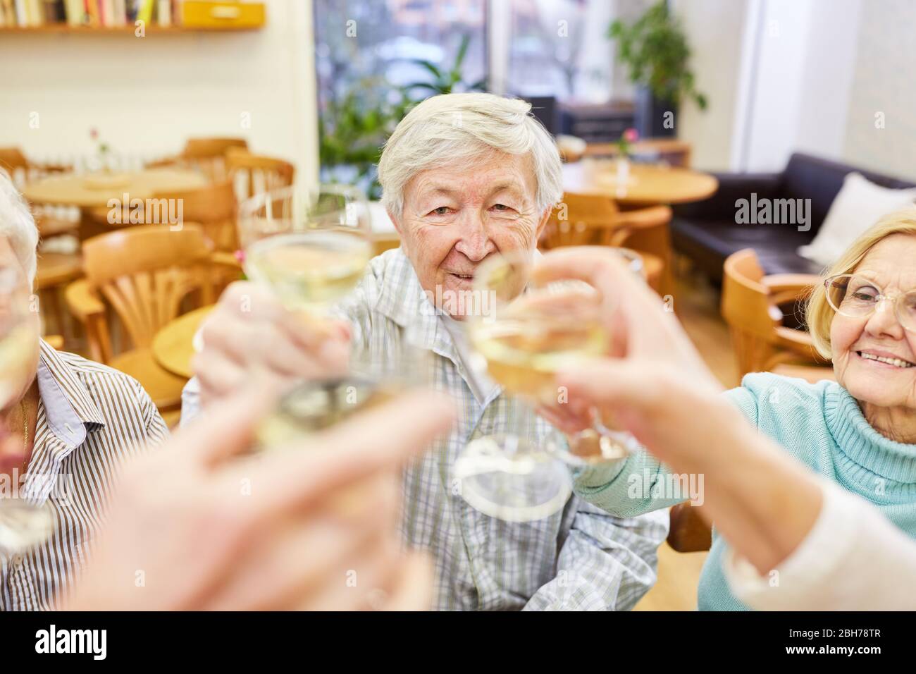 Les aînés toasts avec un verre de vin blanc à une fête d'anniversaire dans une maison de retraite Banque D'Images