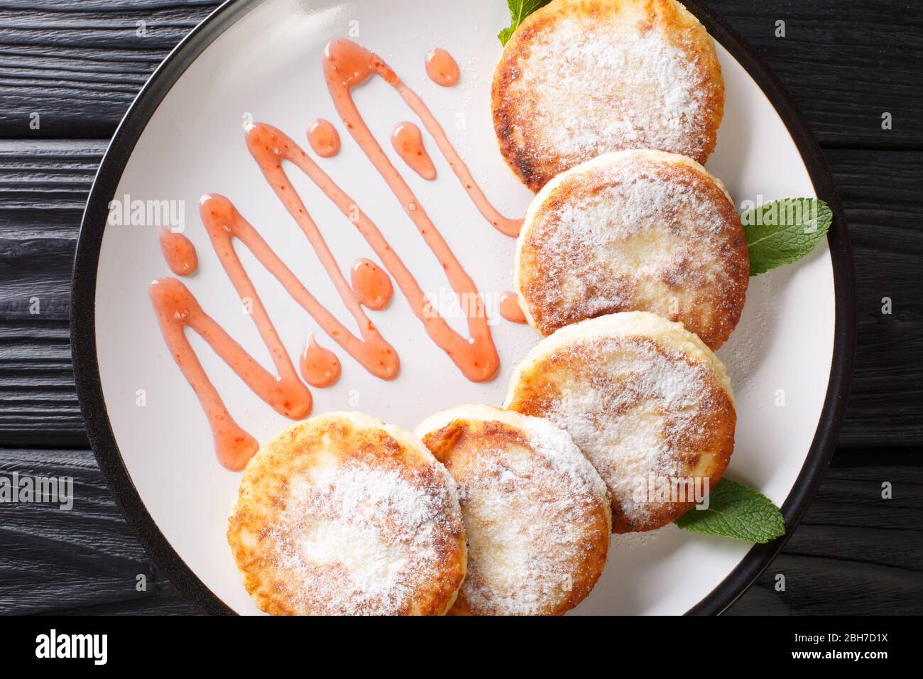 Cuisine ukrainienne syrniki avec sucre en poudre et confiture de fraises dans une assiette sur la table. Vue horizontale du dessus Banque D'Images