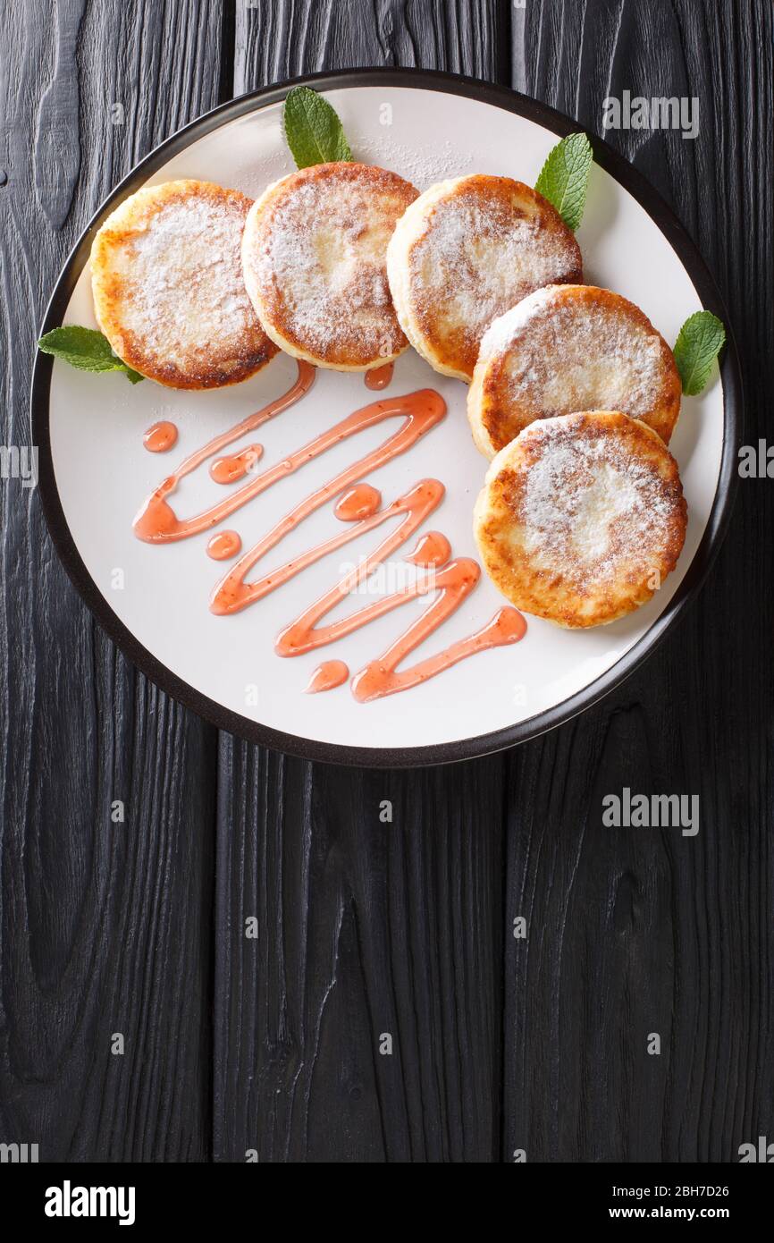 Servir de syrniki traditionnel servi avec de la poudre de sucre et de confiture de baies dans une assiette sur la table. Vue verticale dessus Banque D'Images