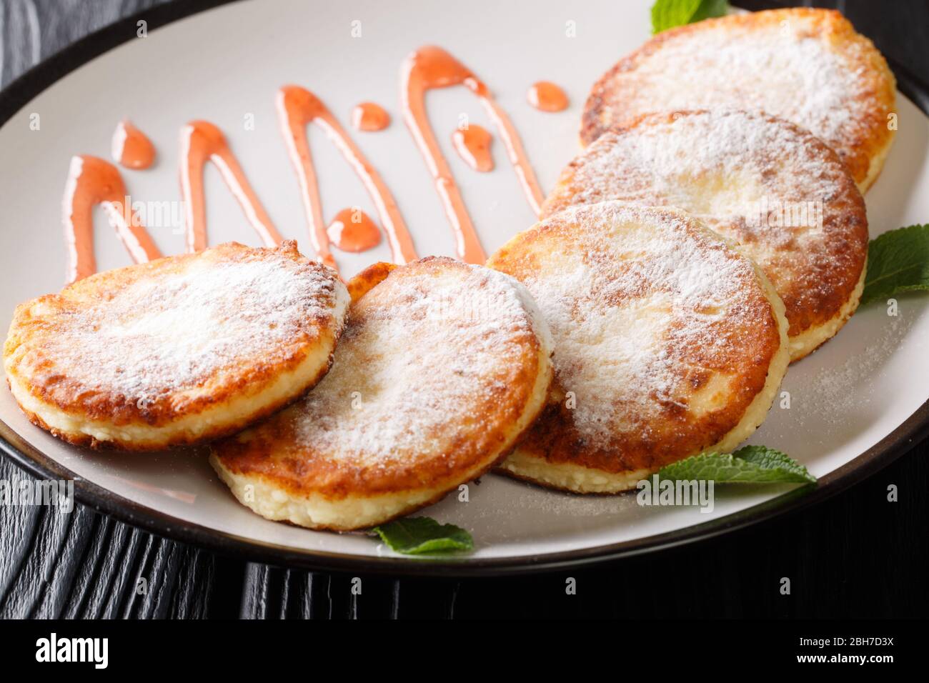 Cuisine ukrainienne syrniki avec sucre en poudre et confiture de fraises dans une assiette sur la table. Horizontale Banque D'Images