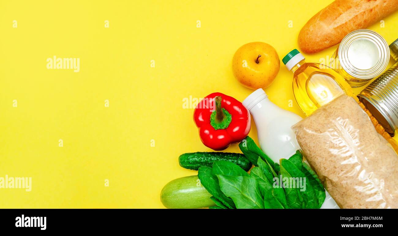 Fournitures alimentaires pour les personnes en isolement sur fond jaune. Produits essentiels : huile, aliments en conserve, céréales, lait, légumes, fruits. Pose plate. Espace de copie Banque D'Images