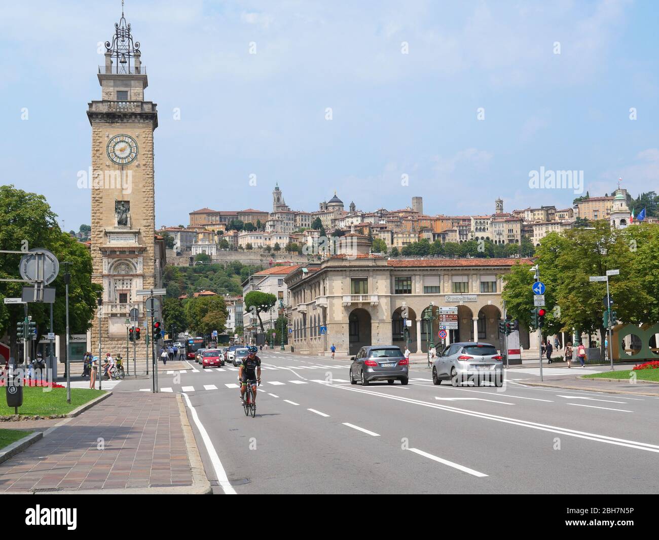 Bergame, Italie - 06 août 2019: Cycliste dans les rues de la partie inférieure de la ville de Bergame avec vue sur la Tour Torre dei Caduti et l'empeigne fortifiée Banque D'Images