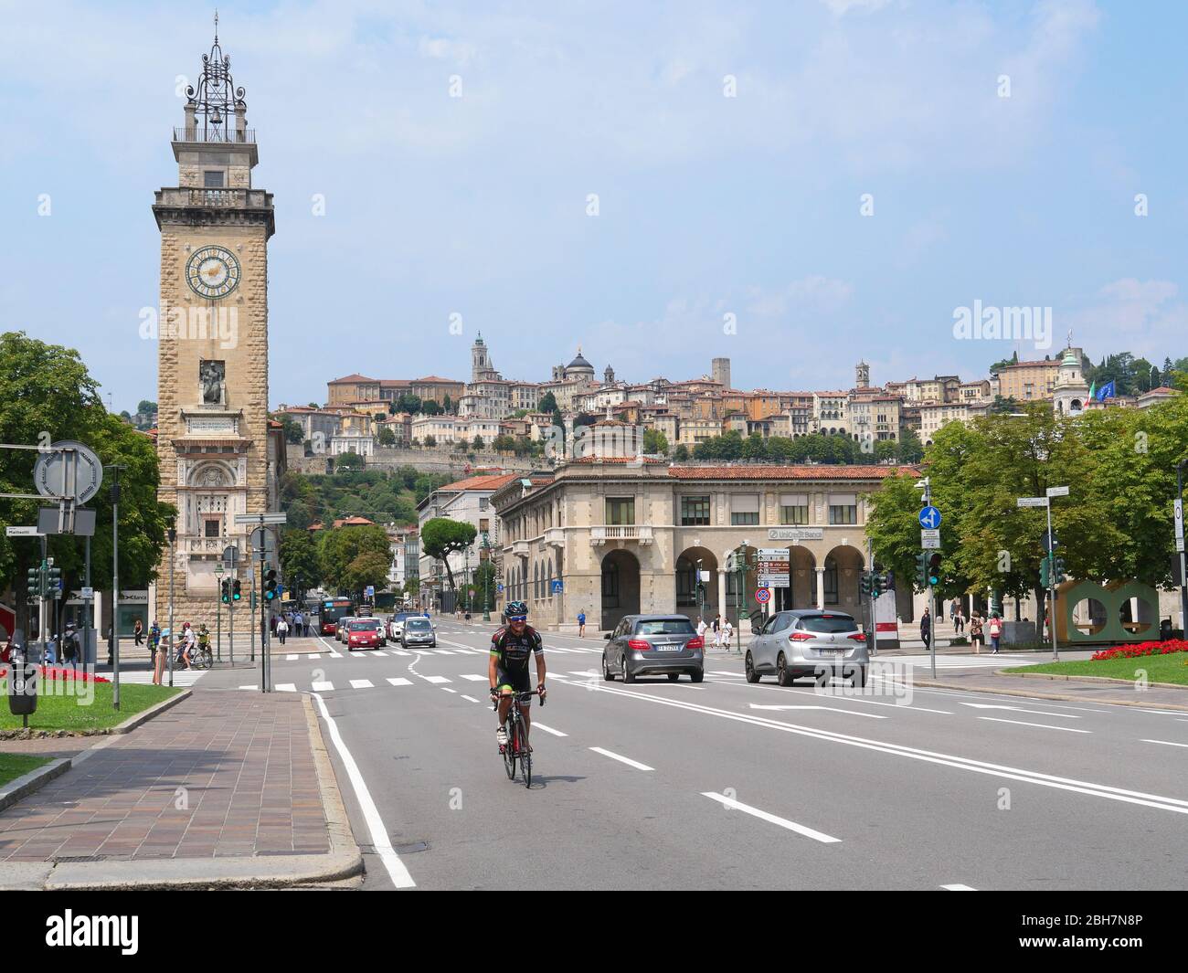 Bergame, Italie - 06 août 2019: Cycliste dans les rues de la partie inférieure de la ville de Bergame avec vue sur la Tour Torre dei Caduti et l'empeigne fortifiée Banque D'Images