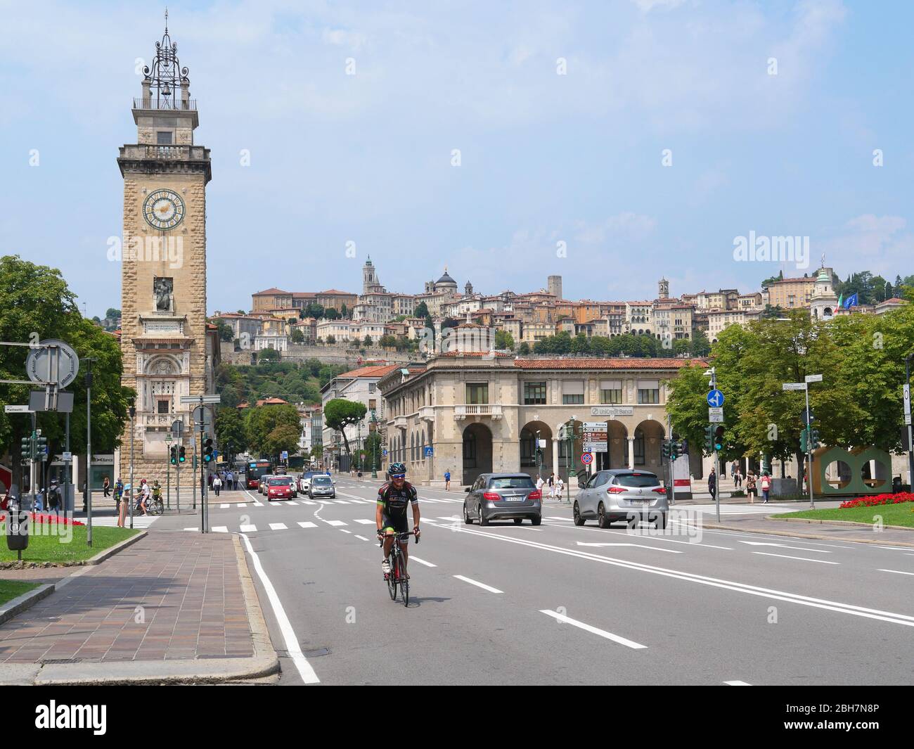 Bergame, Italie - 06 août 2019: Cycliste dans les rues de la partie inférieure de la ville de Bergame avec vue sur la Tour Torre dei Caduti et l'empeigne fortifiée Banque D'Images Bergame, Italie - 06 août 2019: Cycliste dans les rues de la partie inférieure de la ville de Bergame avec vue sur la Tour Torre dei Caduti et l'empeigne fortifiée Banque D'Images