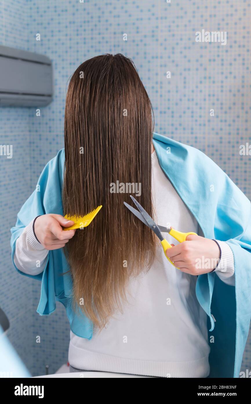 Une belle jeune fille tient un ciseaux pour couper ses cheveux elle-même  pendant le maintien du coronavirus, regardant dans le miroir. Coupe de  cheveux de bricolage pendant l'épidiemi Photo Stock - Alamy