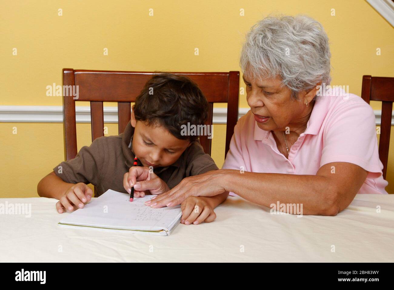 Austin, Texas États-Unis, 22 août 2009: Garçon mexicain-américain de cinq ans pratiquant l'écriture à la maison tandis que sa grand-mère observe et aide. M. ©Bob Daemmrich Banque D'Images