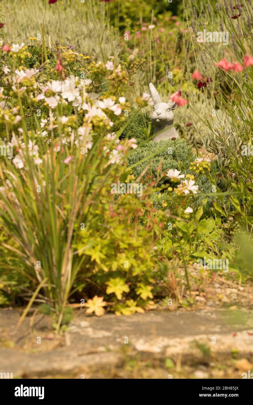 Sculpture de lapin en pierre dans un jardin anglais entouré de fleurs et de graminées Banque D'Images