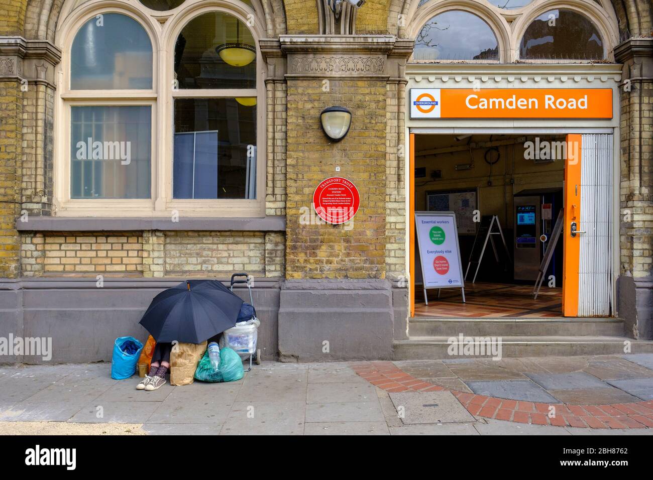 Coronavirus Lockdown, Londres, Camden Town, un sans-abri abrite du soleil, le panneau d'entrée de la gare pour les voyages essentiels seulement Banque D'Images