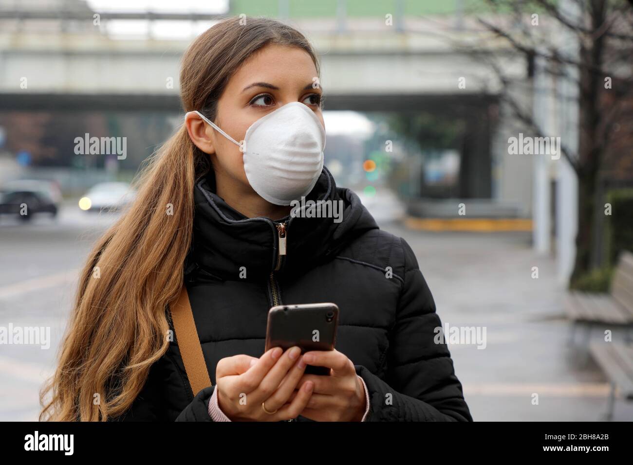 COVID-19 application mobile pandémique de coronavirus - Jeune femme portant un masque facial à l'aide de l'application Smart Phone dans la rue de la ville pour l'aide au traçage de contact dans Respon Banque D'Images