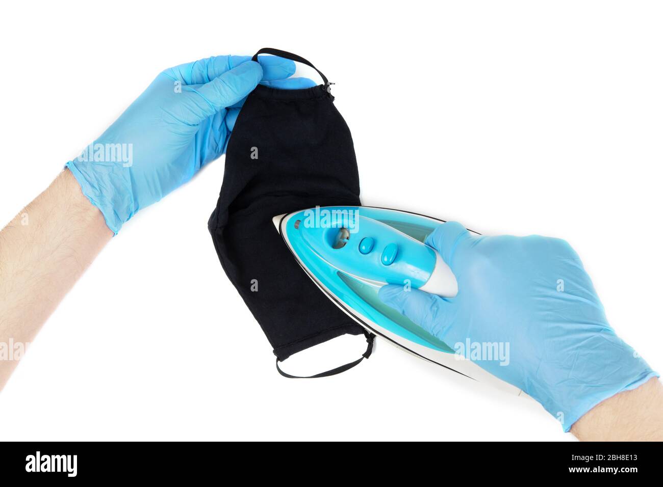 Les mains mâles dans des gants en nitrile jetables bleus sont en fer avec un masque noir réutilisable. Nettoyage du masque en tissu lavable. Vue de la première personne, isolée sur blanc. Banque D'Images