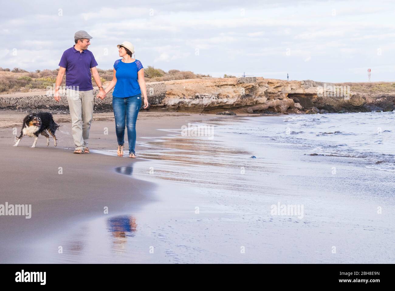 un couple heureux en vacances à pied sur la rive de la plage avec des vagues sur l'océan et une belle bordure de chien collie jouer avec eux. loisirs en plein air pour les personnes amoureux et la famille alternative Banque D'Images