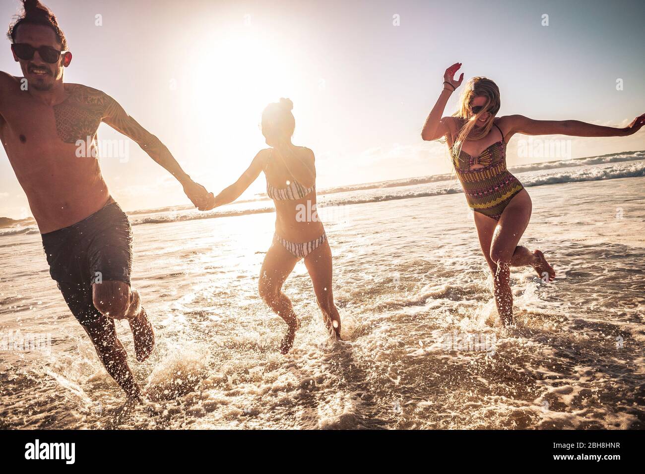 Amis caucasiens groupe de personnes homme et deux femmes apprécient et s'amuser ensemble en amitié pendant les vacances d'été à court de l'eau - coucher de soleil en contre-jour avec ciel clair Banque D'Images