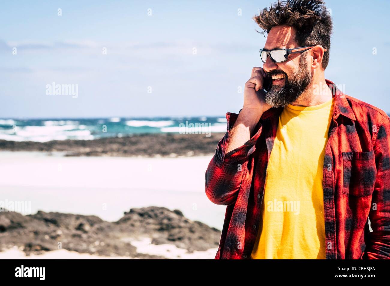 Joyeux homme hipster avec barbe et lunettes de soleil parlant au téléphone  avec des amis dans la Beuitufl extérieur activité de loisirs - concept de  vacances d'été avec plage et océan et