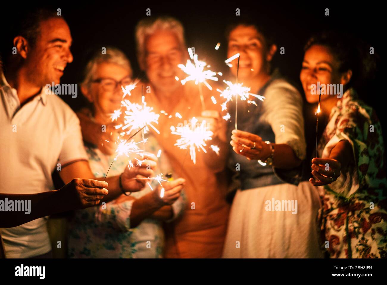 les groupes de gens se réjouissent de célébrer ensemble la veille ou l'anniversaire de la nouvelle année avec des lumières et des feux d'artifice en extérieur d'amitié à l'heure du soir - famille et amis différents âges célèbrent amical et souriant Banque D'Images