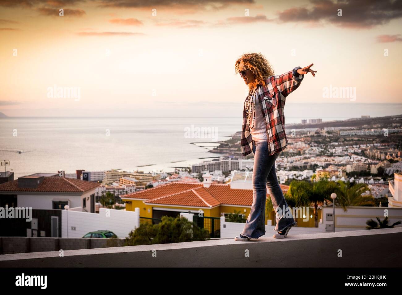 Femme souriante se promenant dans l'équilibre sur une belle vue sur la côte de la ville au coucher du soleil - liberté et indépendance concept de bonheur pour les personnes d'âge moyen profitant d'activités de loisirs en plein air sur les maisons Banque D'Images