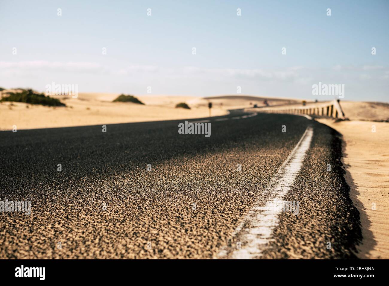 Vue rapprochée du sol sur la route longue en asphalte noir avec dunes de sable du désert sur les côtés - voyage et explorer destination alternative concept de vacances d'été - se concentrer sur la première partie et défocused backgorund Banque D'Images