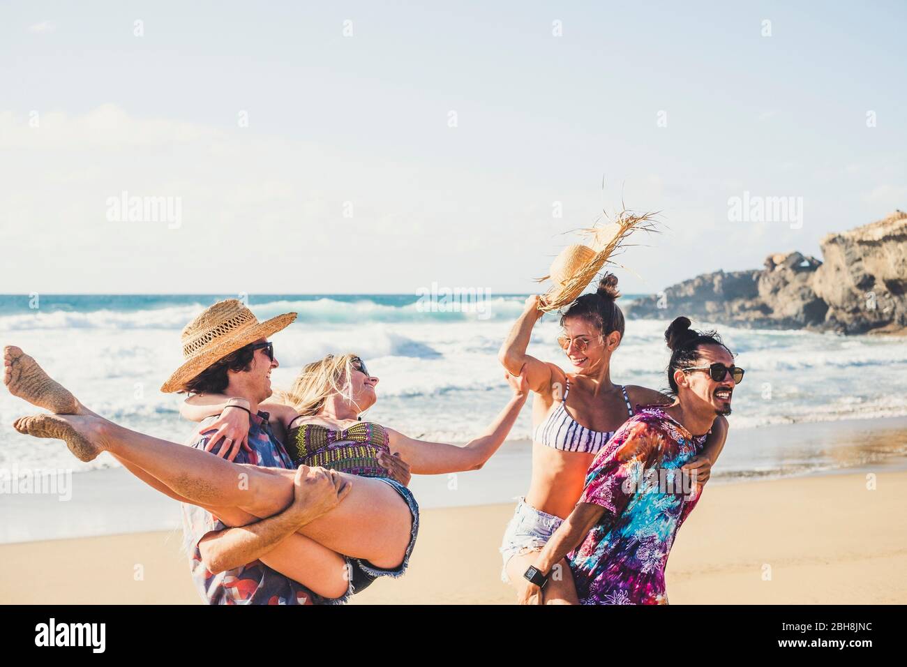 Groupe de personnes gaies les garçons et les filles s'amusent ensemble à la plage pendant les vacances d'été - hommes transportant des femmes - des cloters colorés pour le concept de vie en plein air de la mer Banque D'Images