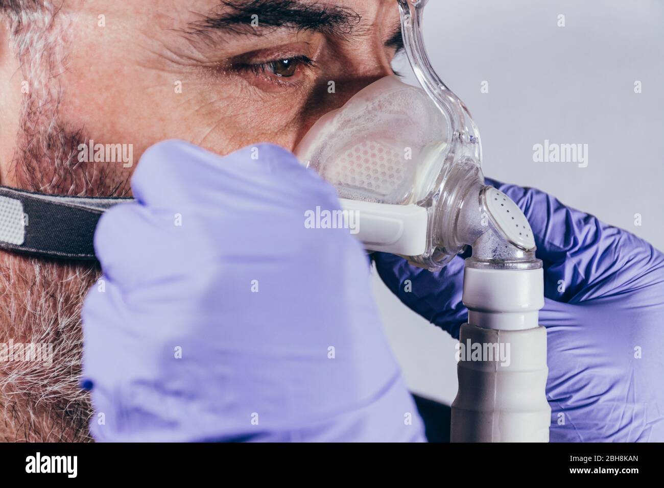 Main avec gant médical mettant sur un homme un masque respiratoire pour les troubles du sommeil. Fond blanc. Apnée. Dispositifs médicaux. Pompe à air. Apnée assistée Banque D'Images