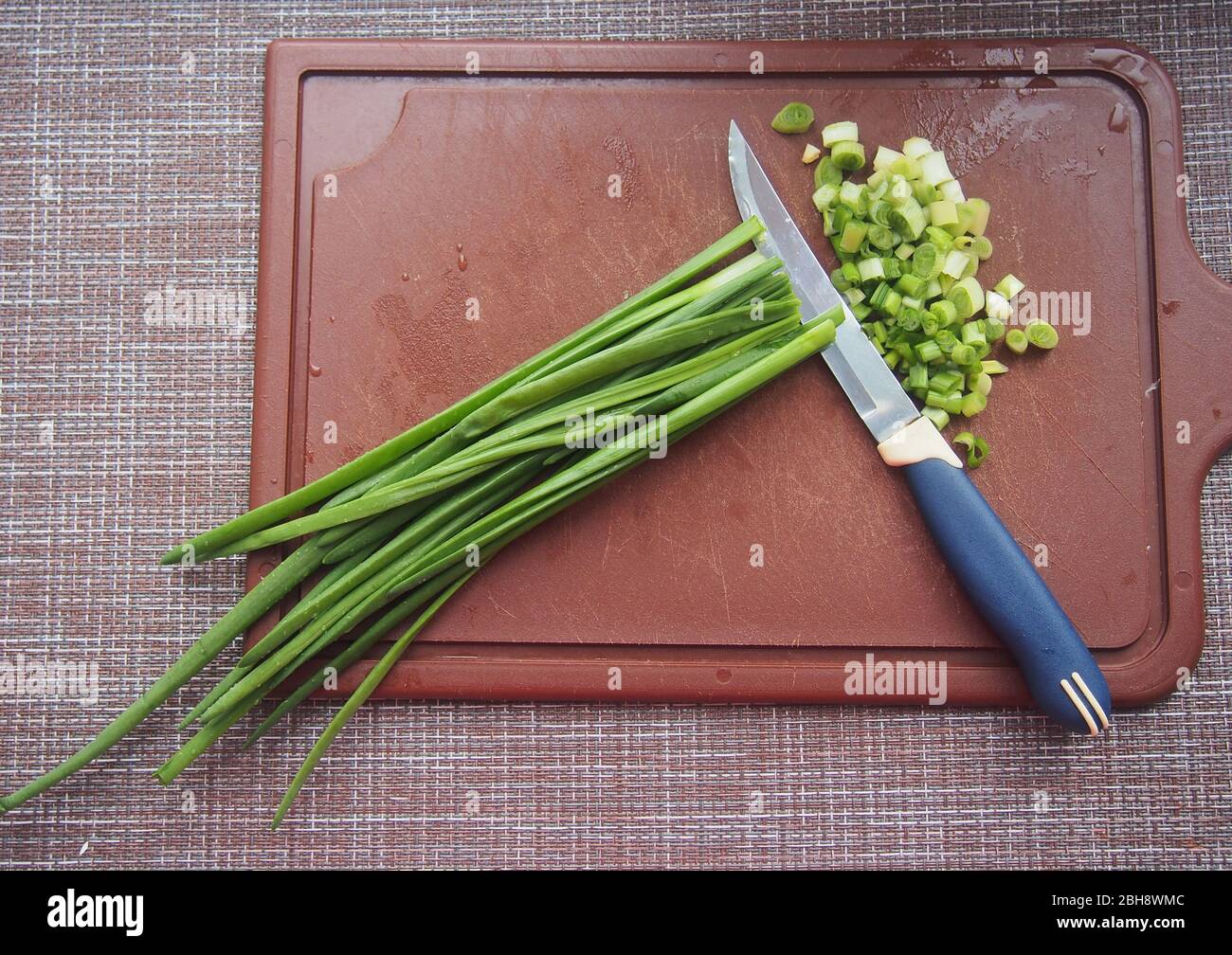 Les feuilles d'oignon et un couteau se trouvent sur une planche à découper en plastique marron. Cuisson. Banque D'Images