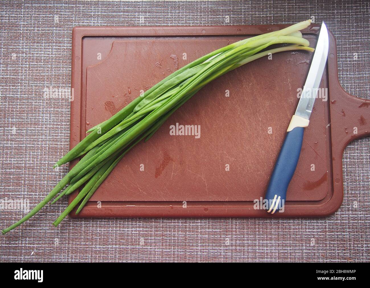 Les feuilles d'oignon et un couteau se trouvent sur une planche à découper en plastique marron. Cuisson. Banque D'Images