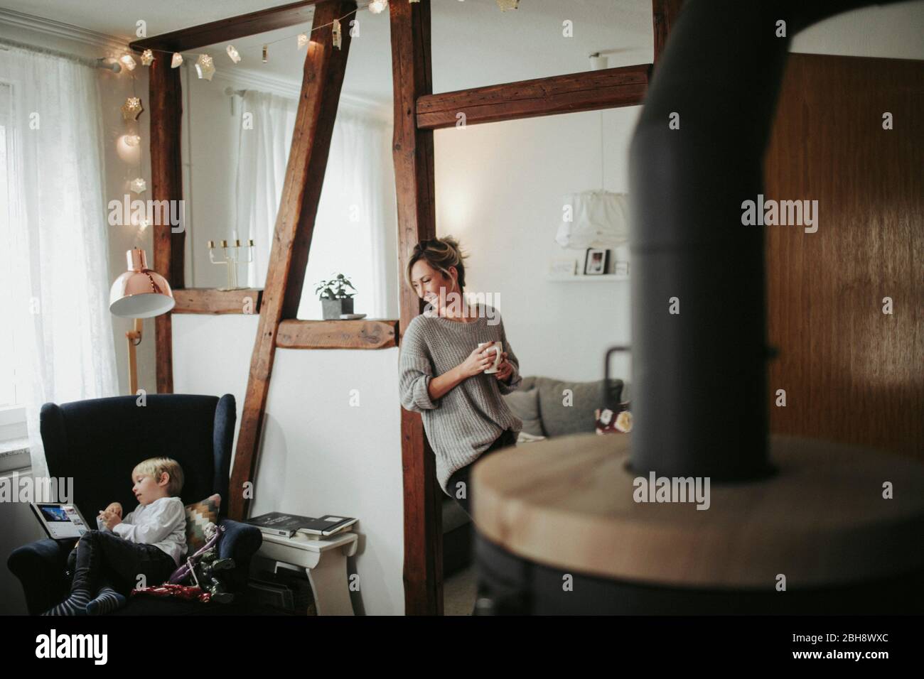 junge Frau in ihrer Wohnung, hält Tasse in der Hand, lächelen, Sohn spielt mit Tablet Computer Banque D'Images