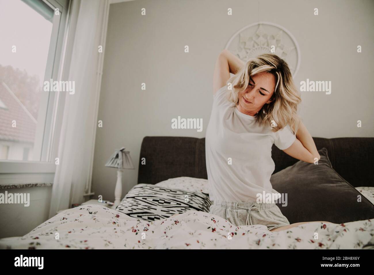 Femme assise dans le lit et s'étire Banque D'Images