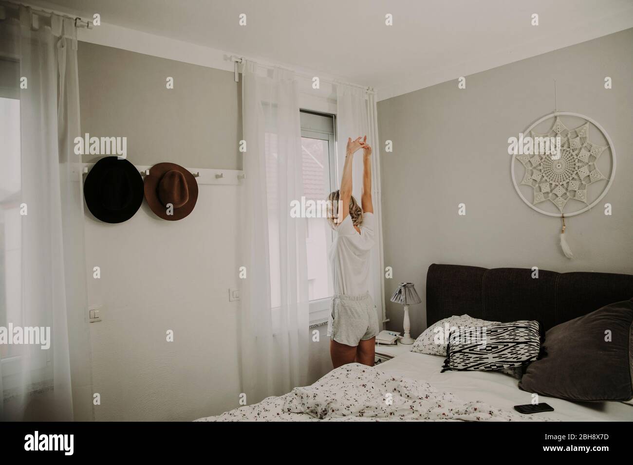 Femme se tient à la fenêtre de la chambre et s'étire, vue arrière Banque D'Images