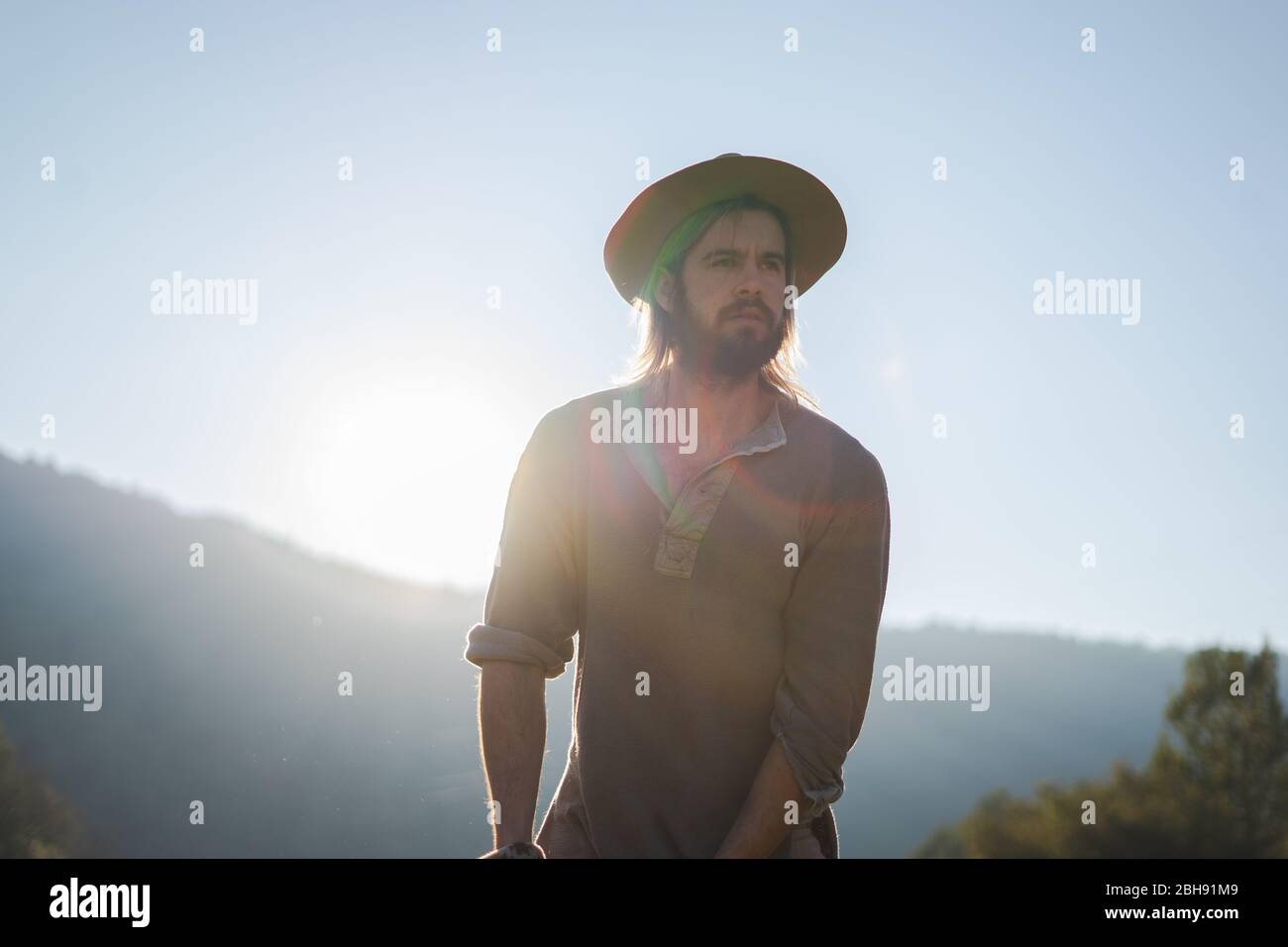 Jeune homme avec une barbe et un chapeau sur un beau coucher de soleil dans les montagnes Banque D'Images
