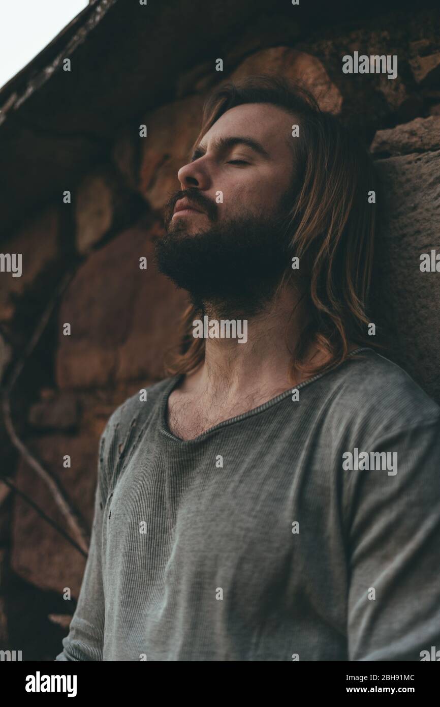 Jeune homme barbu méditant sur le mur de la ferme Banque D'Images