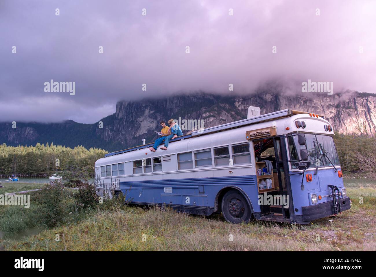 deux personnes assises au sommet de l'école de bus lecture livre devant la montagne Banque D'Images