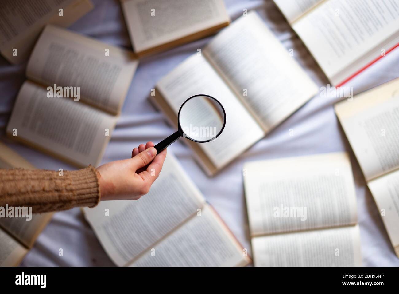 Main avec loupe sur un fond avec des livres. Banque D'Images