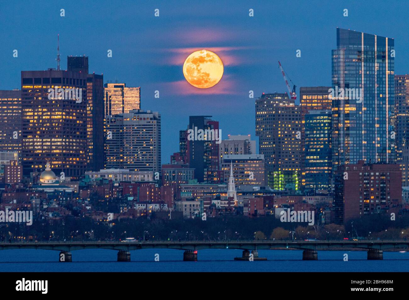 La lune s'élève au-delà de la ville et se situe entre les bâtiments à l'heure bleue. Banque D'Images