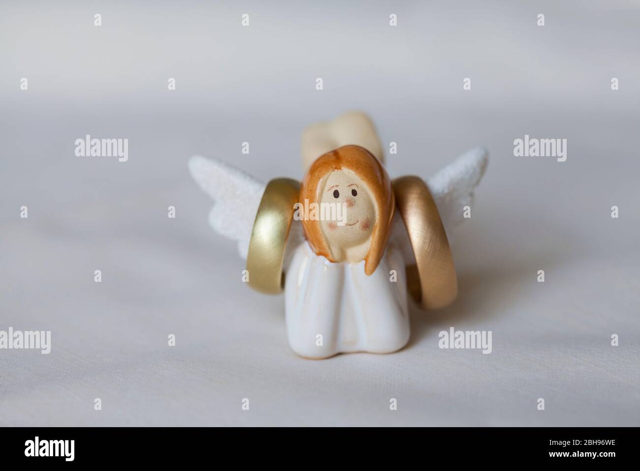 Les anneaux de mariage pendent sur les ailes d'un petit ange figure, fond blanc Banque D'Images