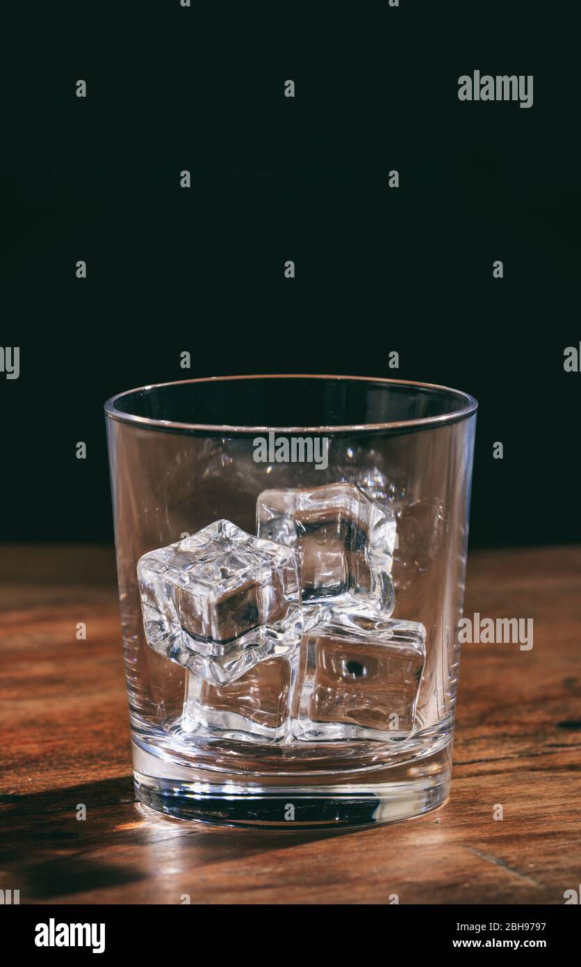 Verre à whisky vide en cristal avec glaçons sur comptoir en bois. Portrait vertical d'un verre transparent transparent transparent et plein de roches de glace sur le noir Banque D'Images