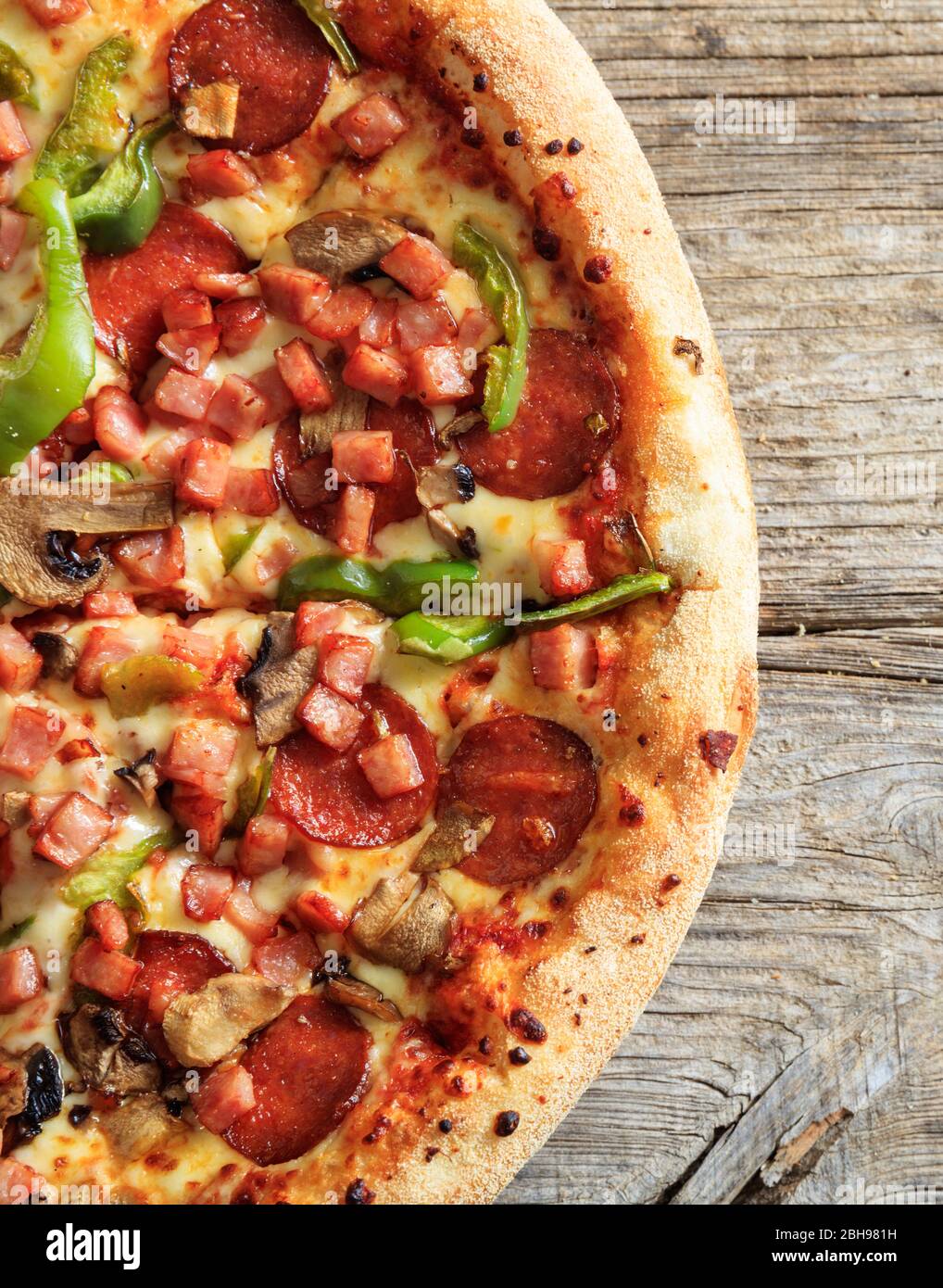 Vue sur la pizza. Demi pizza italienne avec jambon, salami et légumes frais sur table en bois, portrait vertical, vue rapprochée. Concept de restauration rapide. Banque D'Images