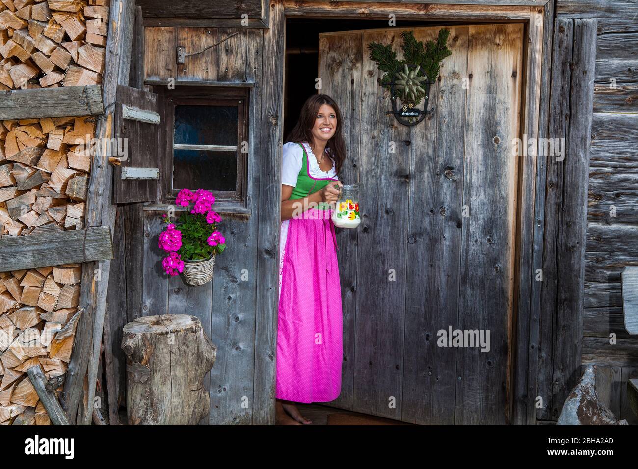 Icyllac Bavaria, jeune femme en robe dirndl avec pichet à lait à l'entrée d'une hutte Banque D'Images