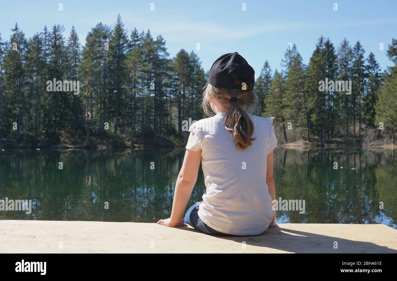 Vue arrière de la fille assise sur un banc donnant sur un petit lac. Banque D'Images