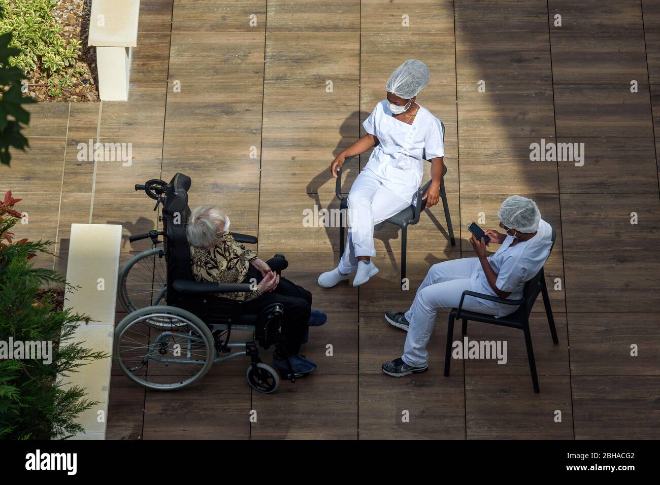 Infirmières et infirmiers s'occupant de personnes âgées dans une maison de soins pendant la pandémie de coronavirus. Les soignants qui ont une pause au soleil avec une vieille femme résidente. Banque D'Images