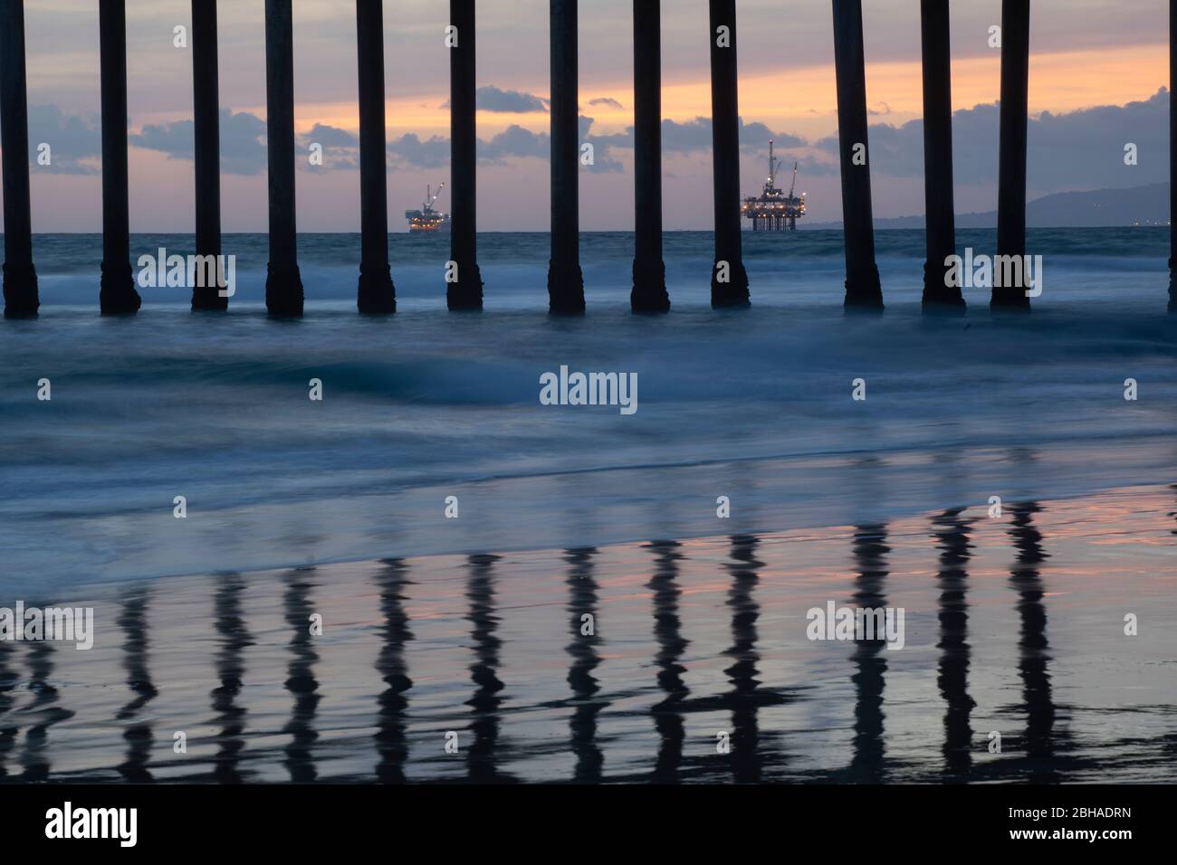 Rigs pétroliers derrière des colonnes de Huntington Beach Pier au coucher du soleil, Californie, États-Unis Banque D'Images