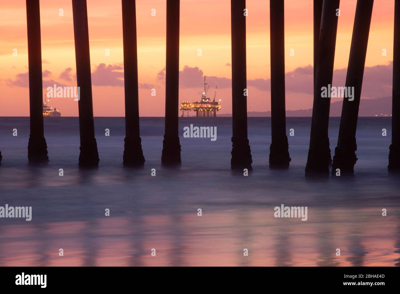 Rigs pétroliers derrière des colonnes de Huntington Beach Pier au coucher du soleil, Californie, États-Unis Banque D'Images
