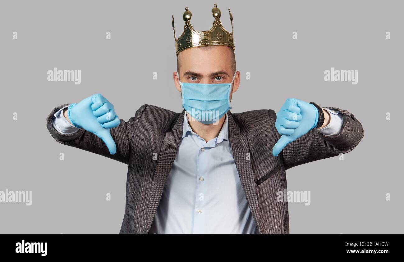 Jeune homme d'affaires dans une couronne et un masque de protection et des gants. Rester à la maison pendant la quarantaine du coronavirus Covid-19. Montre pouce vers le bas Banque D'Images