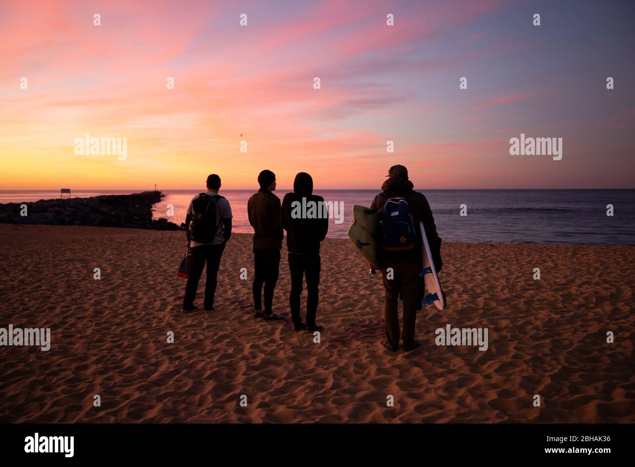 Quatre surfeurs se tenant sur la plage au coucher du soleil, Huntington Beach, Californie, États-Unis Banque D'Images